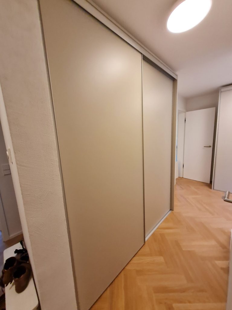 Auf einem polierten Holzboden steht ein Kleiderschrank mit Schiebetüren, der einen modernen und übersichtlichen Stauraum bietet.