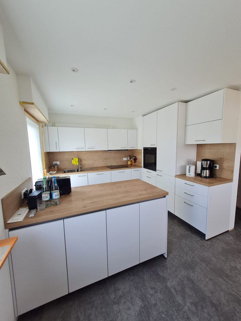 Eine stilvolle Küche mit eleganten weißen Schränken und edlem Holzboden, die ein modernes und gemütliches Design bietet.