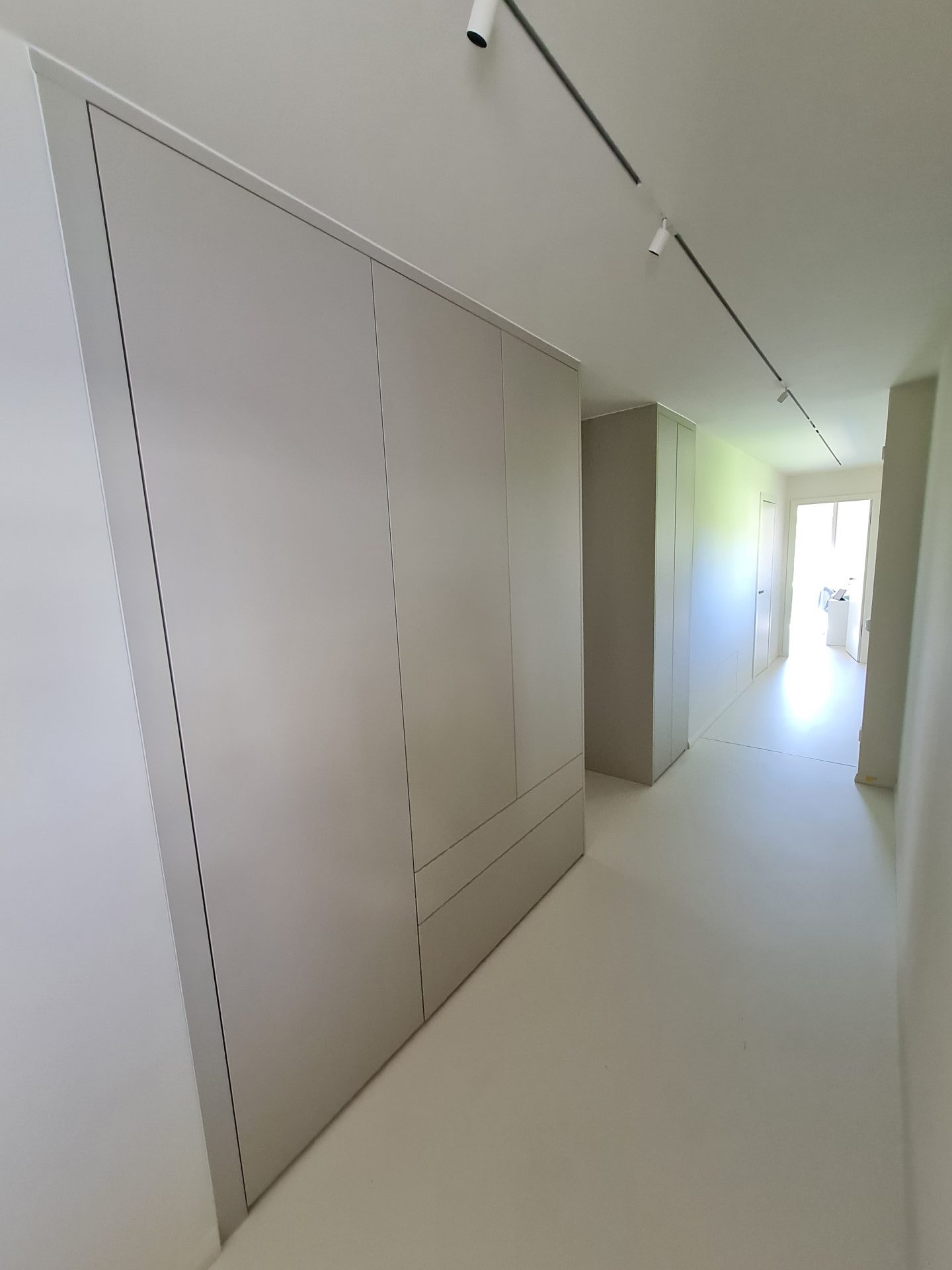 Ein Flur mit weißen Schränken auf der einen Seite und einem Fenster, durch das natürliches Licht in den Raum fällt.