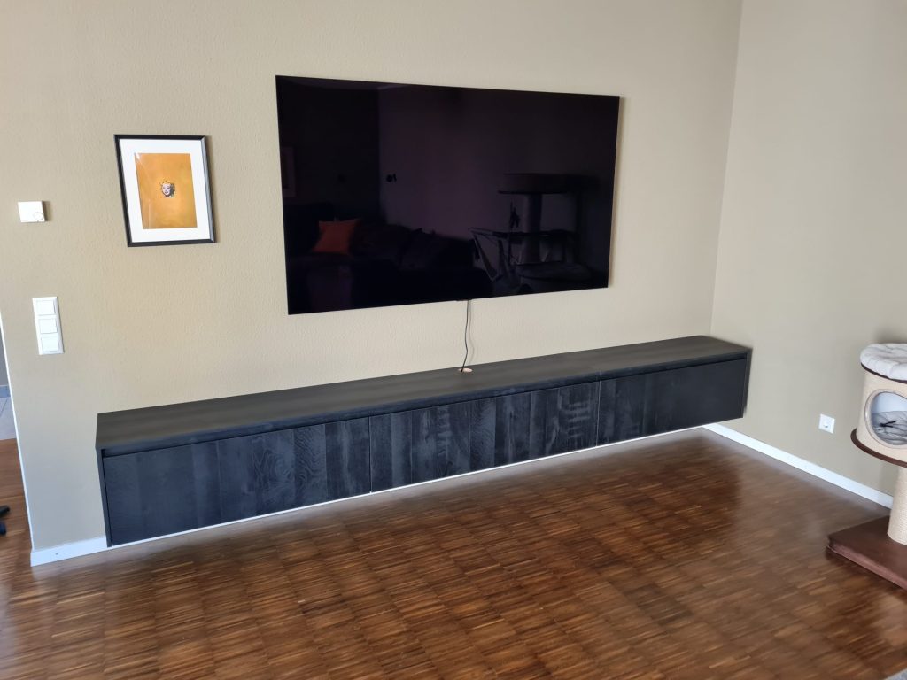 Ein an der Wand montierter Fernseher in einem gemütlichen Wohnzimmer mit neutralfarbigen Wänden und einem bequemen Sofa.