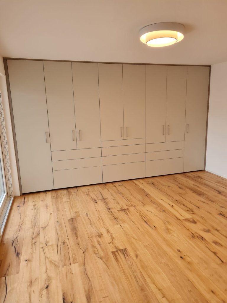 Ein moderner Kleiderschrank mit Schiebetüren steht auf einem edlen Holzboden und unterstreicht die stilvolle Organisation des Wohnraums.